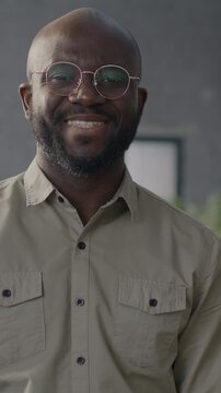 Slow motion portrait of cheerful young African American man standing in workplace in office smiling looking at camera. Job and career concept.