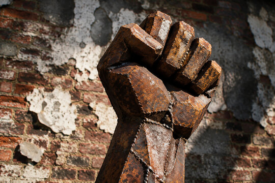 Sculpture of a clenched fist made from welded rusty metal against a peeling brick wall.