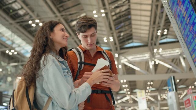 Caucasian couple looking at flight information display board in airport terminal. 
