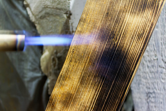 Close-up of a gas torch flame charring a wooden board to create a rustic texture and provide natural wood protection through a traditional shou sugi ban flame treatment technique