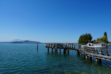Obraz premium peaceful pier scene on a lake with boats and trees, serene lakeside with mountains in the background, still scene of nature and tranquility, looking out at the calm water and distant hills.