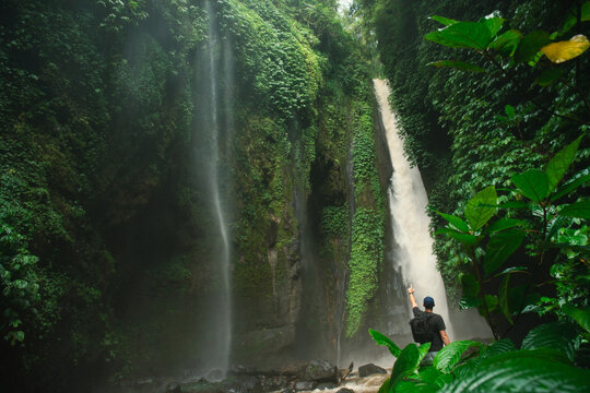 A traveler admires a tall waterfall in lush greenery