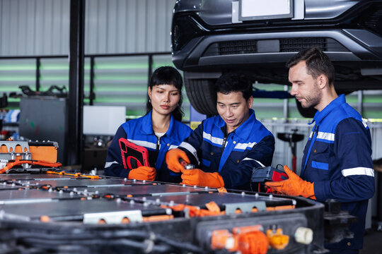 Three automotive technicians take part in practical training on electric vehicle battery inspection.Wearing blue uniforms and orange gloves, they demonstrate component checks beside an exposed battery