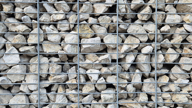 A gabion wall filled with light grey and beige stones behind a metal wire mesh grid.