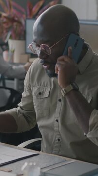 African American businessman involved in professional conversation talking on mobile phone and reading document in office. Business and communication concept.