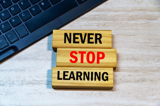 Never Stop Learning text written on wooden blocks next to laptop keyboard on wooden office desk background. Continuous education concept.
