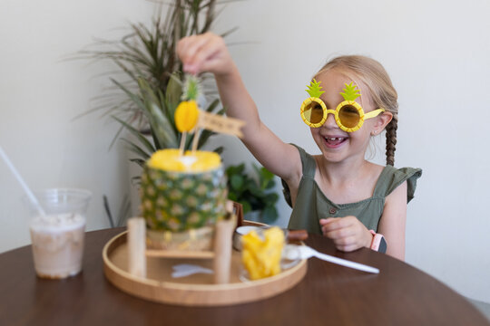 Happy child wearing pineapple glasses helping prepare tropical snack at home