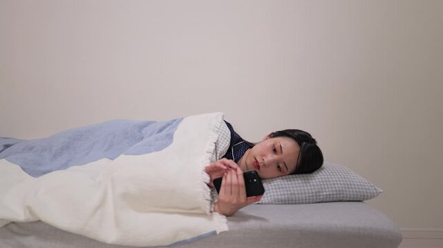 モーニングルーティン：ベッドに横たわりスマートフォンを見る女性