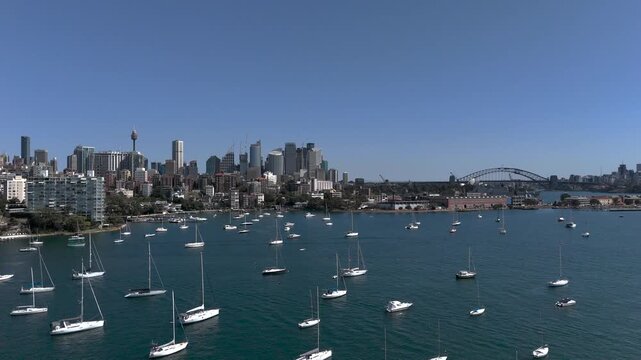 Sydney skyline from aerial view on beautiful sunny day. Camera descends from high to low altitude looking across to Sydney Harbour Bridge, Elizabeth Bay and CBD. Yachts and Motor Boats inn foreground.