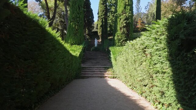 Steps on the shady alleys of Santa Clotilde Park in Lloret de Mar, Costa Brava, Spain - paths among green trees and bushes, statues