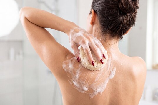 Woman washing her back with a loofah sponge in the shower