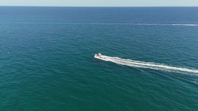 An aerial drone view of a motorboat riding high-speed waves near the town of Lloret de Mar on the Costa Brava, Spain, on a sunny summer day.