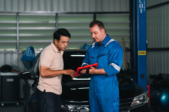 Ev car battery cells service Automobile mechanic and customer inspecting car in repair garage with diagnostic tablet and focused expressions