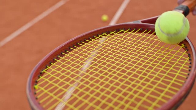 Tennis racket bouncing yellow ball on clay court in slow motion. Footage suitable for sports equipment advertising, athletic training campaigns and fitness promo