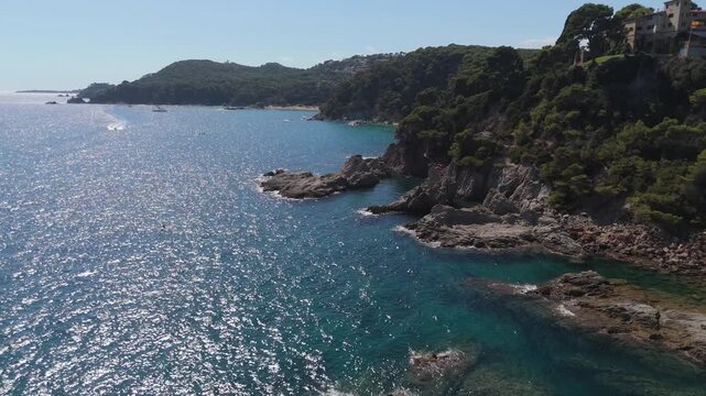 An aerial view of a drone flies over the beach, sea and coastal cliffs near Santa Clotilde Park on a sunny day in the tourist town of Lloret de Mar, Catalonia, Spain