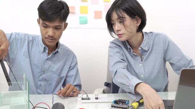 Young Asian woman and man using microcontroller to monitor water quality.