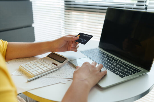 Asian Woman holding a credit card while using a laptop and calculator at home, representing debt management, budgeting, digital banking, expenses and personal financial planning.