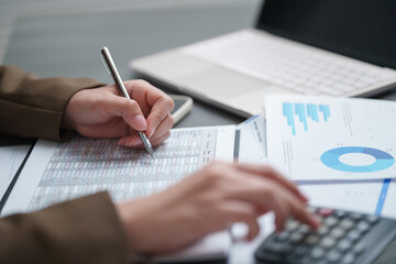 Businesswoman calculating and reviewing financial reports with charts and data at an office desk,...