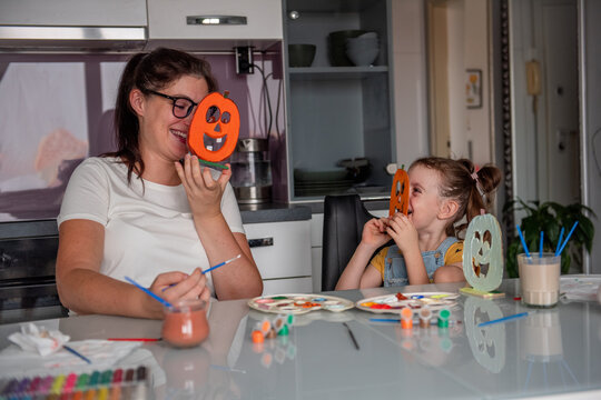 Smiling other and daughter play with diy pumpkin masks at home
