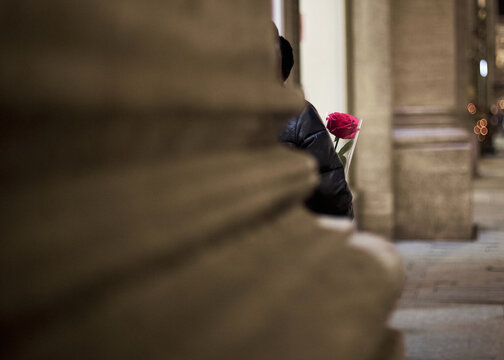 Person hiding behind column with red rose in city