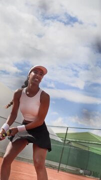 Vertical video of young adult Biracial woman hitting ball with racket during tennis training on outdoor court. Footage suitable for fitness app advertising, sports brand campaigns