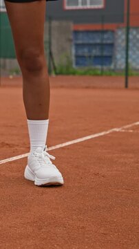 Vertical video of tennis ball bouncing on clay court near foot of female athlete in slow motion. Ideal for athletic footwear advertising and sports social media content