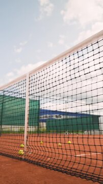 Vertical video of yellow tennis balls rolling on clay court near net in slow motion. Footage suitable for sports tournament promotions and athletic coaching campaigns