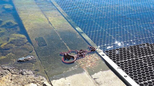 rusty metal chain and ring, partially submerged in shallow water at the edge of a concrete ramp or dock. river Orb. Valras, France