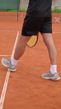 Vertical tracking shot of CaucBiracial male tennis player walking on clay court with racket in slow motion. Ideal for sports gear commercials, athletic coaching promos and fitness marketing