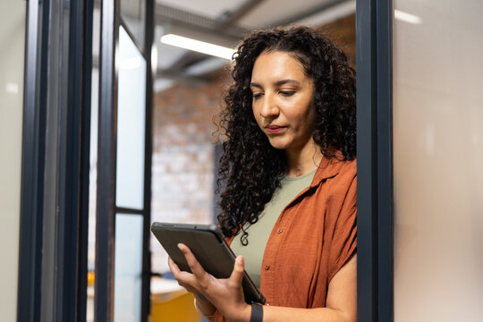 African American woman standing in office holding tablet, wearing rust top and smartwatch
