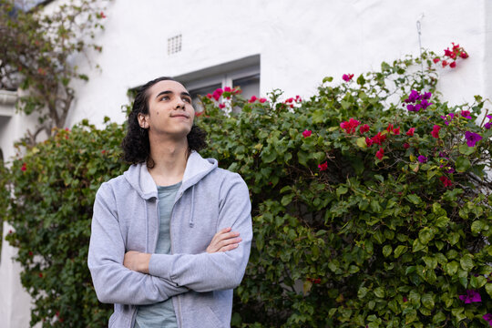 African American man 20s standing left of frame by bougainvillea hedge in gray hoodie, copy space