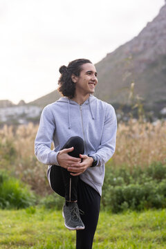 African American man balancing on left leg holding knee at foothill, wearing hoodie, wrist device