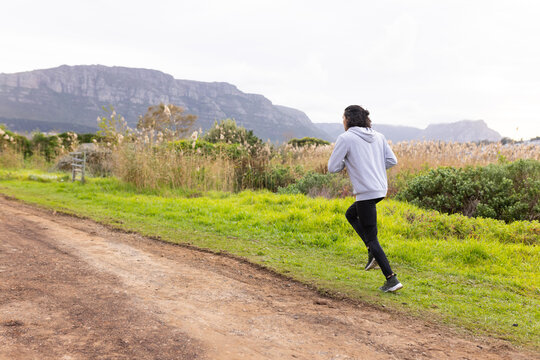 African American man jogging gray hoodie, black tights on dirt trail passing metal gate, copy space
