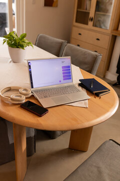 Open silver laptop is displaying chat interface on round table in home with headphones and phone
