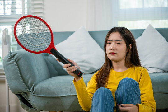 Asian female sitting floor using mosquito device swatter or electric net racket