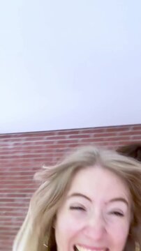 Happy young caucasian couple laughing and joking while recording a selfie video, with the man playfully pretending to bite his girlfriend's shoulder in a moment of pure fun and happiness
