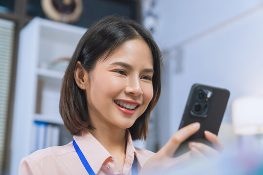 Smiling young Asian businesswoman using smartphone while working in office, mobile communication and business technology concept.