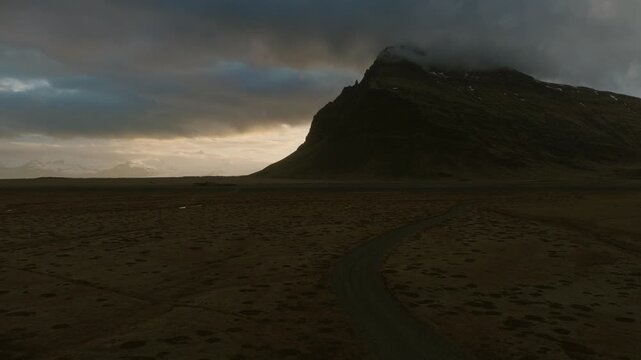 Lomagnupur rises above Skeidararsandur in Skaftarhreppur, Southern Region, Iceland, with dark glacial channels and volcanic terrain beneath dramatic cloud cover, drone forwad flyover.