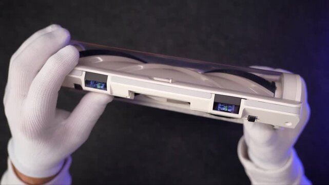 White gloved hands inspecting and assembling white plastic components of a modern vacuum cleaner appliance mechanism on a clean surface indoors