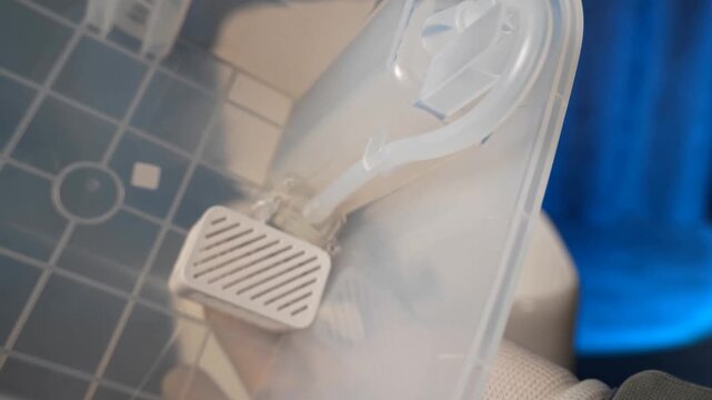 Transparent plastic water tank container of a robotic vacuum cleaning station with internal tubing and filter components showing internal plumbing details for automated maintenance