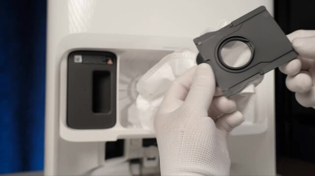 Standard white disposable dust bag removal from the interior compartment of a modern automated cleaning device docking station during routine household maintenance operations