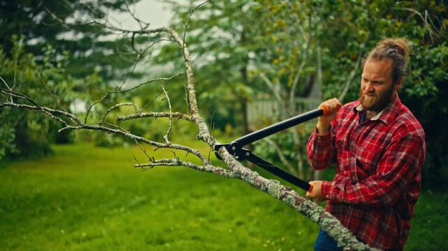 A man uses extendable loppers to cut a tree branch in rural Norway