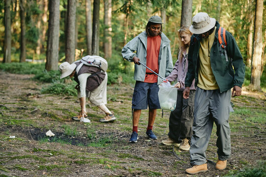 Diverse young adult friends collecting plastic waste in forest. Multiethnic volunteers cleaning up nature reserve, promoting environmental conservation and eco friendly lifestyle