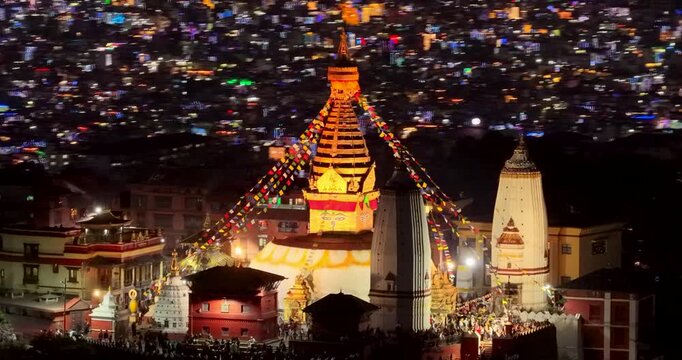 Kathmandu, Nepal, Aerial shot of the golden spire and temples of Swayambhunath Monkey Temple brightly lit against the glowing backdrop of city lights during the Tihar festival.