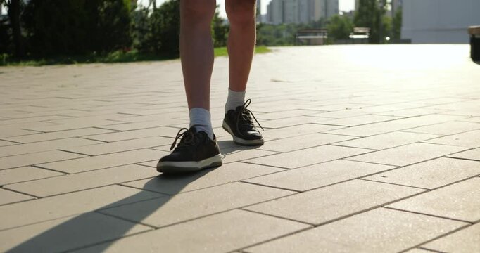 Young person walking on sunny pavement. Bright day creates cheerful atmosphere. Footsteps echo in park setting. Outdoor leisure activity promotes healthy lifestyle.