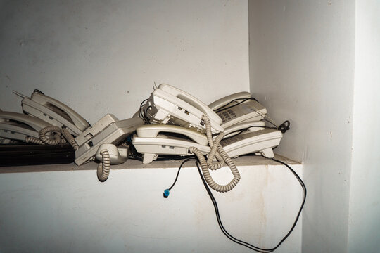 Old telephones stacked on dusty corner shelf