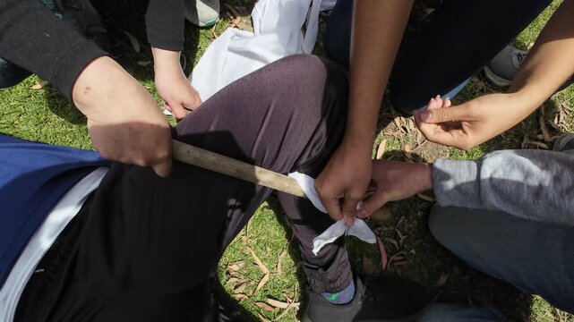 Group of people providing first aid by applying a makeshift splint and bandage to an injured leg