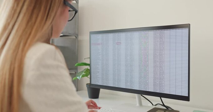 Analyst woman reviews spreadsheet data on monitor. Finance accounting professional in office analyzes a database for analytics on a widescreen display. Strong focus and accuracy concept.