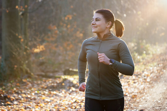 A young, cheerful, athletic woman in winter sportswear jogging, running and training outdoors on a early autumn morning	