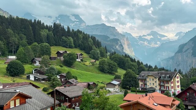 Wengen village chalets cover a green hillside above Lauterbrunnen Valley, Swiss Alpine homes overlook forests cliffs and distant snow covered peaks